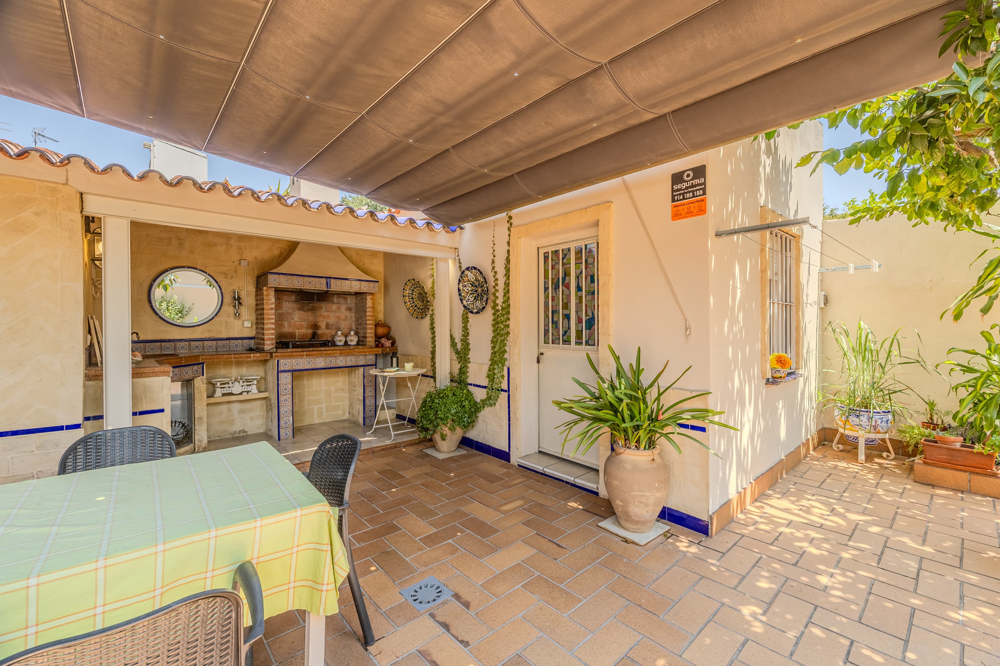 Mesa de comedor exterior bajo pérgola y barbacoa de obra en el patio privado